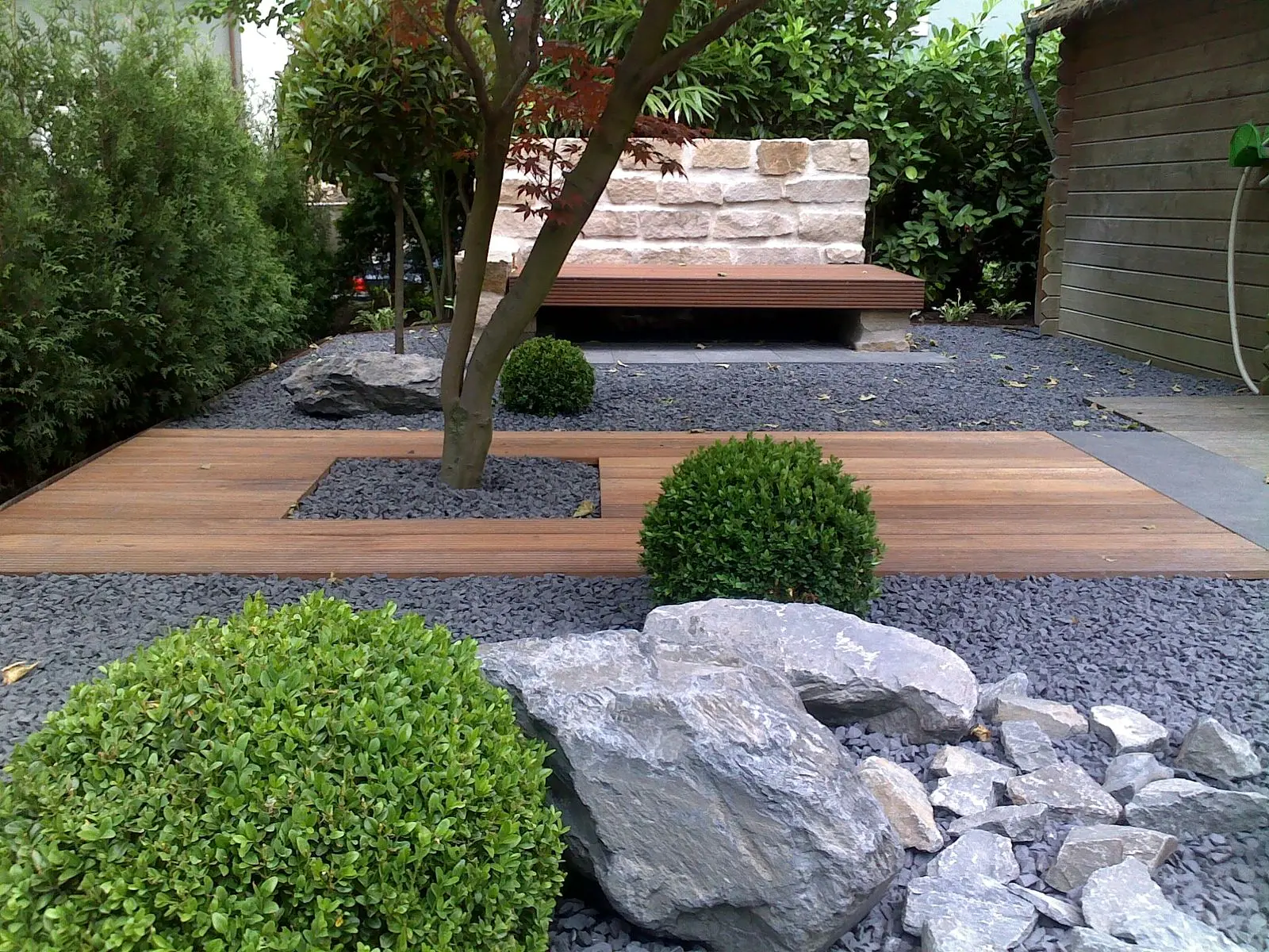 Breite Natursteinfläche mit Holzsteg im Garten