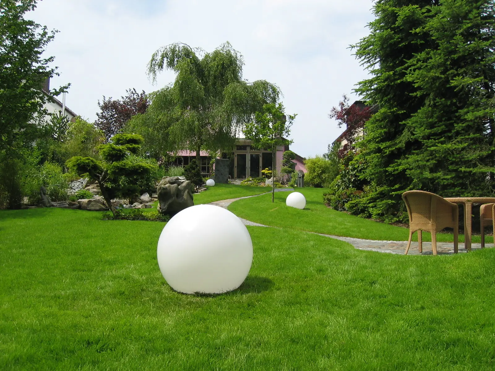 Grüner Gartenraum mit weißen Kugelobjekten und Sitzplatz