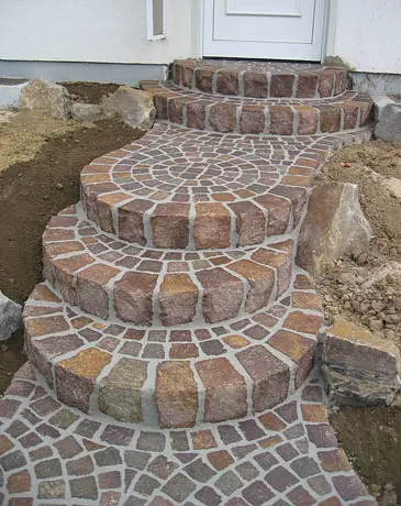 Geschwungene Eingangstreppe aus rötlichem Natursteinpflaster